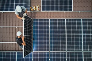 Men technicians mounting photovoltaic solar moduls on roof of house. Electricians in helmets installing solar panel system outdoors. Concept of alternative and renewable energy. Aerial view.